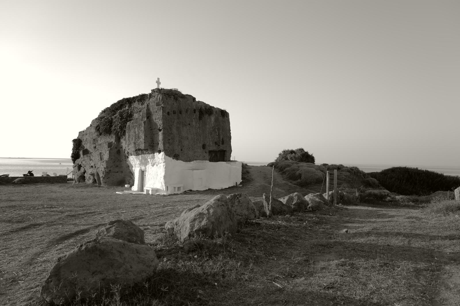 A rock-cut chapel with a white base on a headland at dusk