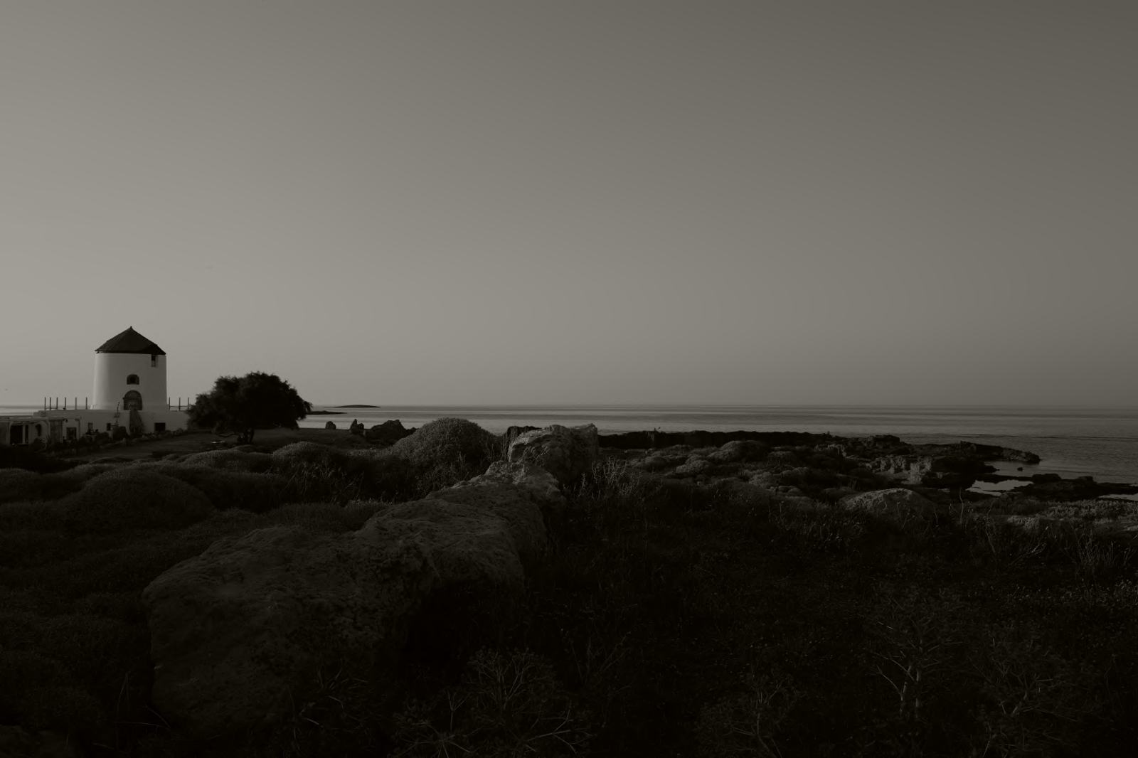 A white windmill above a rocky shore at dawn