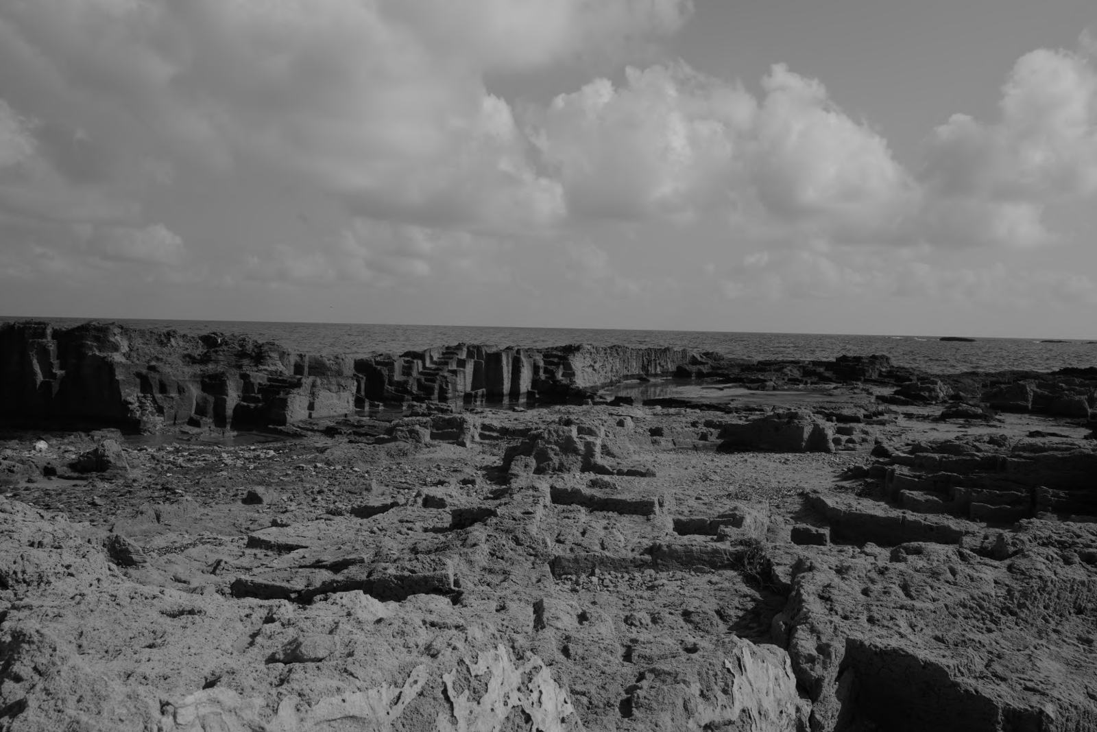 Rock cut in rectangular blocks beside the sea under clouds